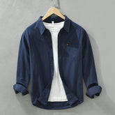 Herren Freizeithemd Dunkelblau aus 100% Baumwolle offen getragen als
Overshirt über einem weißen T-Shirt auf einem Holzbügel. Cheapseasons
Japanese Fresh Style.