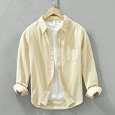 Herren Freizeithemd Cremefarbig aus 100% Baumwolle offen getragen als
Overshirt über einem weißen T-Shirt auf einem Holzbügel. Cheapseasons
Japanese Fresh Style.